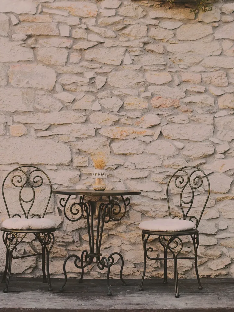 Hand-bent wrought iron bistro table and two chairs against a stone wall
